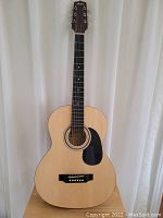 Front view of a Montana acoustic guitar showing natural wood top, black pickguard, and six-string setup (one string missing).