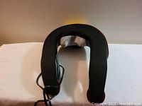 Top view of the U-shaped neck massager showing black fabric exterior with slight red trim and gray mesh interior