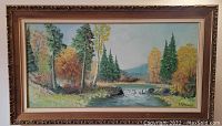 Full view of the framed oil painting showing a river in the woods with a small waterfall and autumn colored trees.