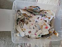 Plastic container filled with old postage stamps still affixed to pieces of envelopes and paper, totaling about 1 kilogram.