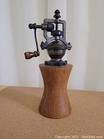 Front view showing curved wooden body with metal grinding mechanism and hand crank with wooden handle.