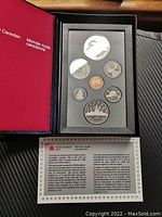 Opened red and black Royal Canadian Mint box displaying seven proof coins in black foam insert with certificate below