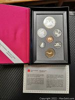 Photo of the full set open in black casing with seven coins displayed in foam slots and certificate card underneath.