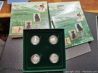 Overview photo of the coin set box, booklet and four coins displayed in green velvet insert, showing packaging and condition of the lot.