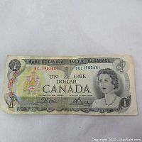 Front side of the 1973 Canada one dollar bill showing Queen Elizabeth II and Canadian coat of arms, with serial number and denomination visible.