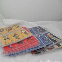 Overview of multiple plastic sleeves holding yellow, red and blue tallboy cards laid flat on white surface
