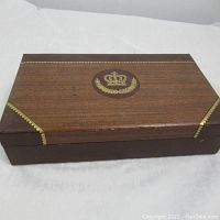 Closed view of rectangular jewelry case with wood grain top and brown faux leather sides, decorated with gold crown emblem and trim