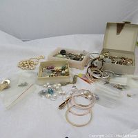 Full view of assorted costume jewelry laid out including pearl necklace, hoop earrings, and boxes with various small jewelry pieces.