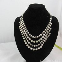 Full view of five-strand silver-tone necklace with rhinestones on black display stand