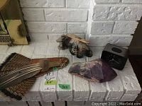 Photo showing two carved art pieces, amethyst stone, black clock, and feather fan on white brick surface