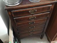 Photo showing six drawers on wooden cabinet with detailed metal handles, one drawer partly open.