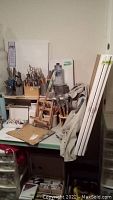 Overview of tabletop with brushes in holders, wooden easel, smock draped and stacked canvases