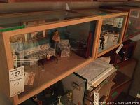 Side view showing living room diorama with floral sofa and three standing figurines behind plexiglass wooden frame.