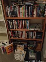 Full view of shelves filled with DVDs from various TV shows and movies, also showing DVDs stacked at bottom with some papers and a DVD player on the shelf.
