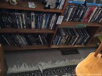 Four wooden shelves filled with DVDs in cases and sleeves, showing a large collection mainly consisting of action and drama movies with some series.