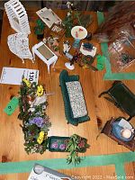 Top view of miniature garden furniture, figurines, and planting arrangements on wooden table.