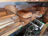 Shelf filled with stacked wooden plaques of different shapes including octagonal, rectangular, and oval plaques along with some small boxes or bases beneath them.
