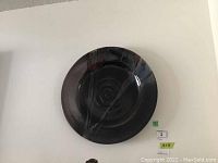 Top view of large dark glossy pottery plate with maroon and green painted streaks and spiral pattern in center