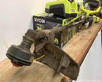 Close-up of the string trimmer head with guard showing dirt and used condition.