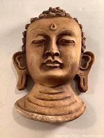Carved wooden Buddha head wall hanging shown from front with serene facial features and ear pendants