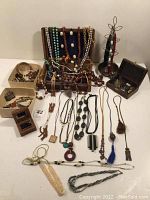 Full view of collection showing necklaces draped over wooden display, multiple boxes filled with jewelry, and a tall metal jewelry holder with earrings.