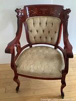 Front view of upholstered arm chair showing tufted fabric backrest and cushion seat on carved wooden frame with casters.