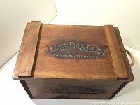 Top and front view showing Jack Daniels logo stamped on lid and front panel of wooden crate with rope handles.