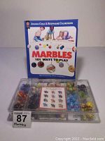 Full view of the marble storage case alongside the instruction book titled 'Marbles 101 Ways to Play' by Joanna Cole and Stephanie Calmenson.