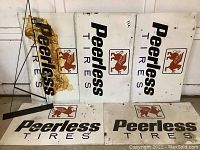 All five rectangular Peerless Tires metal signs arranged on the floor showing full logos and some rust wear.