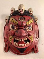 Front view of the red painted Mahakala mask showing the facial features, eyes, teeth, and skull details on the headdress.