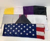 Four folded flags laid flat, including the American flag and three pride flags with various color stripes.