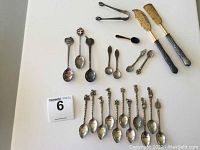 Full collection of 22 silver and silver-plated spoons and utensils including cheese tools, collector spoons, sugar tongs, salt spoons, and demitasse spoons.