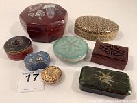 Overview of 8 vintage and decorative trinket boxes in various shapes and materials on white background.