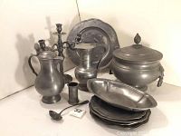 Overview of the entire pewter set including plates, tureen, pitchers, candelabra, clock, tankard, and ladle.