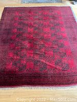 Full view of red and navy blue wool carpet with geometric pattern, laid flat on wooden floor.