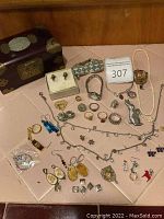 Full view of assorted jewelry collection spread on a flat surface showing rings, earrings, necklaces, pendants, charms, and a small rabbit figurine along with a wooden jewelry box.