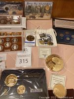 Various US coin proof sets and commemorative coins displayed on table, showing multiple protective cases including commemorative gold-toned coin sets and proof set holders.