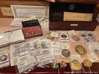 Multiple collectible coins and certificates including Bradbury Mint box, American Mint coins, certificates in view.