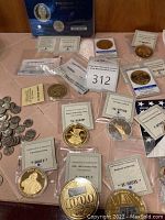 Overview of multiple coins including gold-toned and bronze-toned commemorative coins and certificates of authenticity, displayed on a surface.