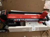 Overall right-side view of log splitter in original foam packaging, red beam, black frame, cardboard box in background.