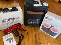 Photo showing the Dynamo handheld steam vacuum cleaner in red with its box and attachments, black EdenPURE heater, and box for a heated foot massager.