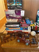 Stacked board games including Trivial Pursuit Genus III, Double Trouble, Monopoly, Word Yahtzee with wooden toys and game accessories in front