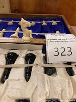 Close-up photo showing hand carved cream colored knight chess piece and black bishop chess pieces inside blue velvet-lined wooden storage box.