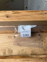 Close-up of 2x6 lumber showing wood grain with auction tag #590 and '1/2' written on it.
