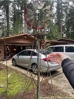 Full view of large metal windmill garden decoration outdoors with person’s hand showing size