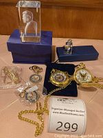 Photo showing entire lot including two pocket watches, two keychains, small gold-tone souvenirs, and Lucite JFK paperweight arranged on table.