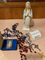 Full lot showing silver bar in case, Madonna statue, and multiple rosaries on a tile surface