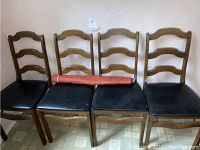 Set of four wooden ladder back chairs with black vinyl seats and visible paint splatter marks. Chairs are stacked side by side against a wall.