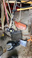 Photo showing assorted gardening tools, rakes, shovels, garden cultivators, and Worx jaw saw on the floor