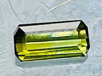 Emerald-cut green tourmaline on reflective surface with pin for scale